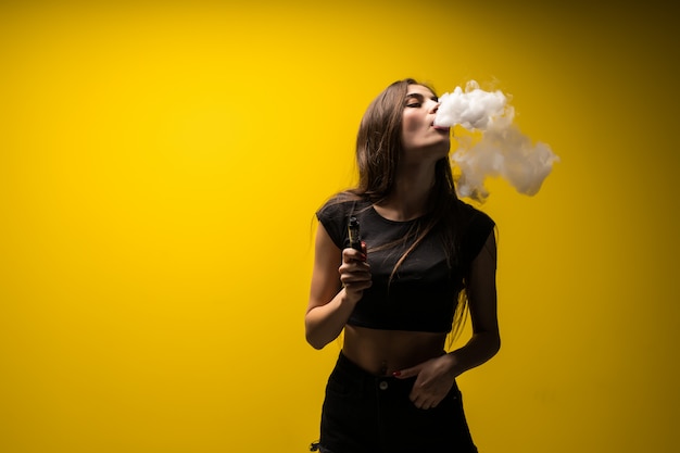 Free Photo attractive woman standing and vaping on yellow wall.