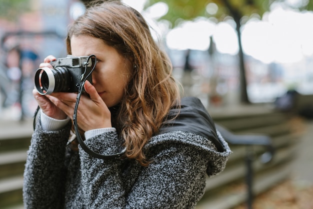 Free photo attractive woman standing wearing a gray coat and taking a picture with a vintage camera