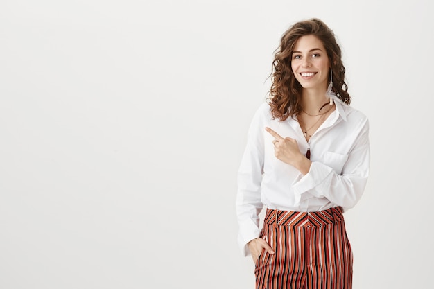 Attractive woman in stylish outfit pointing left