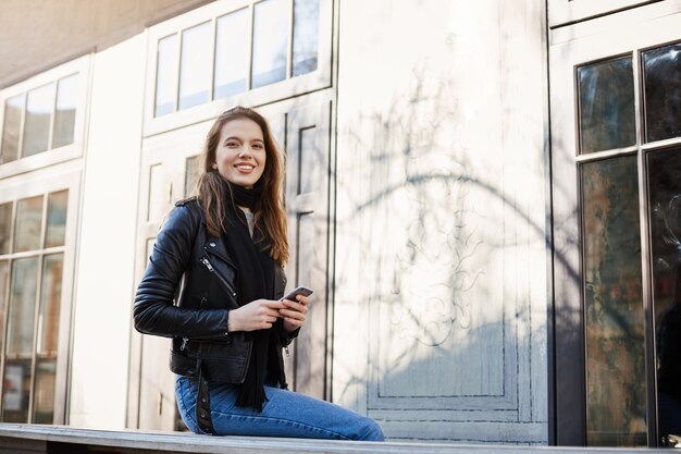 Attractive woman walking in city, sitting near cafe, laughing over funny guy who tries impress her, holding smartphone.