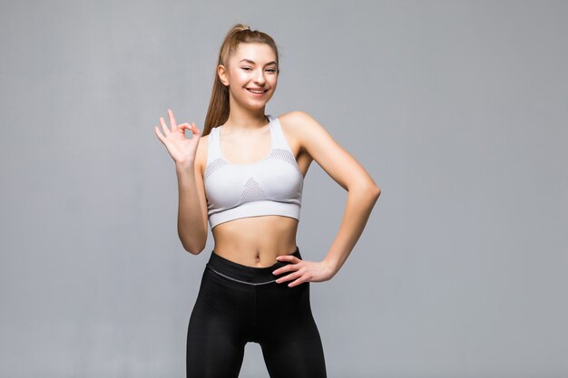 Attractive woman with okay in gym attire in her outstretched arms isolated