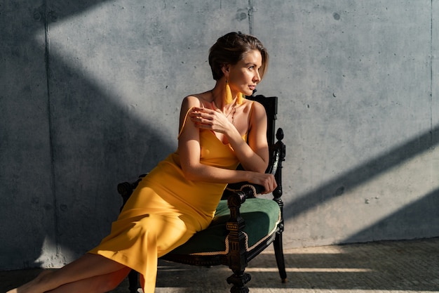 Free photo attractive woman in yellow summer dress with short hairstyle in interior room concrete wall background posing, sunny shadows