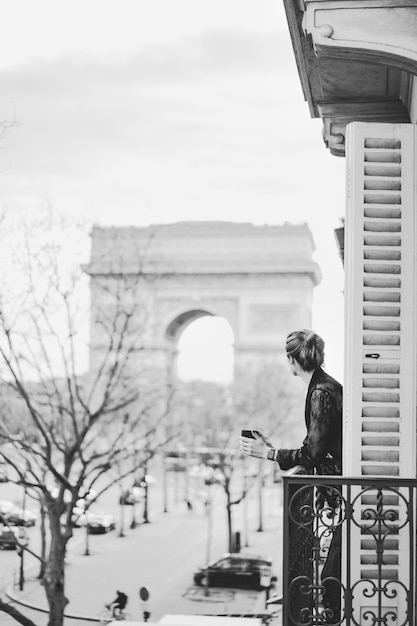 Attractive  yang woman in pajama is drinking coffee on balcony in the morning in city Paris. view of the triumphal arch.