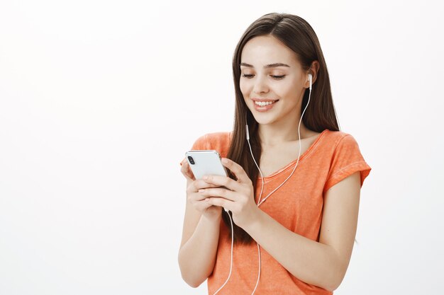 Attractive young brunette girl listening music in headphones and texting, using mobile phone, enjoying interesting podcast