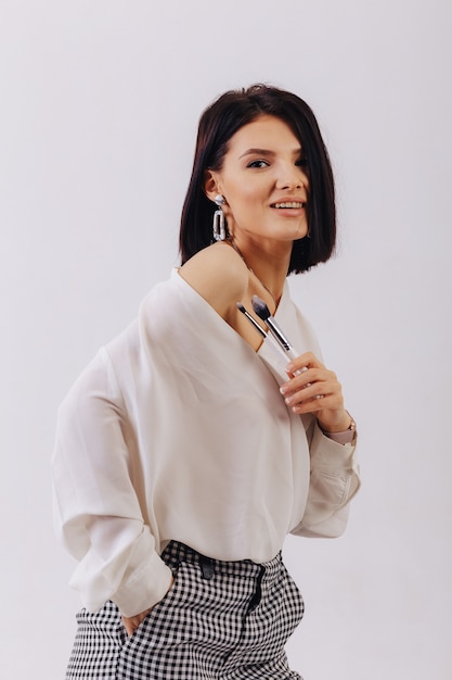 Attractive young business girl with makeup brushes posing on plain background. concept of makeup and cosmetics.