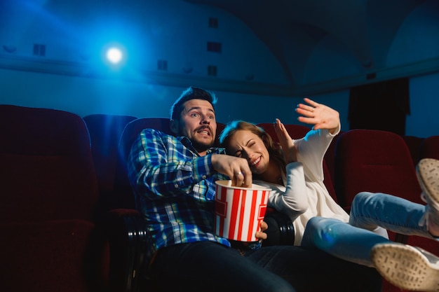 Free photo attractive young caucasian couple watching a film at a movie theater, house or cinema. look expressive, astonished and emotional. sitting alone and having fun. relation, love, family, weekend time.