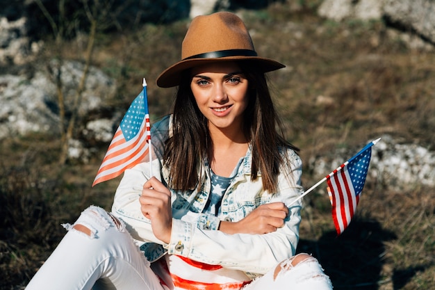 Attractive young female sitting with American flags on nature