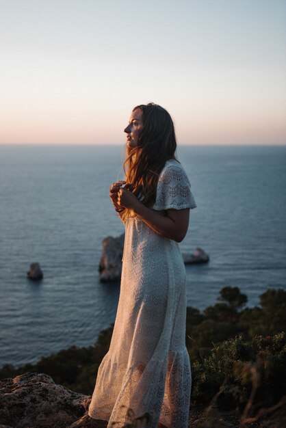 An attractive young female with a beautiful white dress walking by the sea in the evening