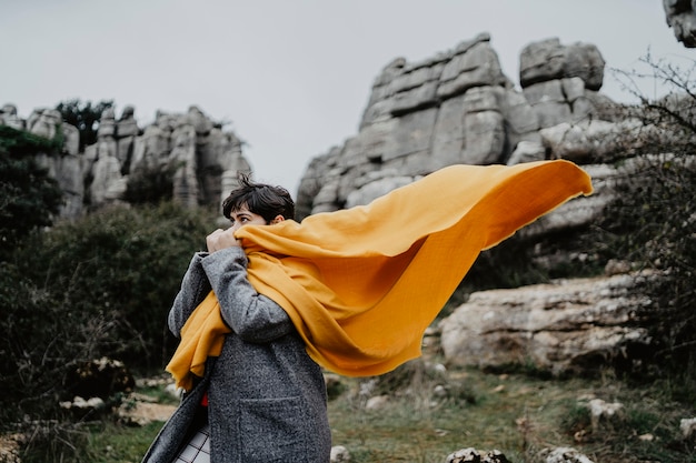 Attractive young female with a coat and a yellow scarf near high rocky cliffs