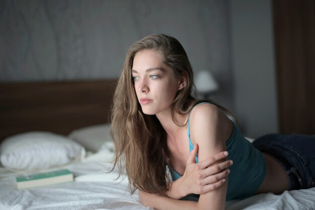 Attractive young female with long hair lying on the bed under the lights in a room