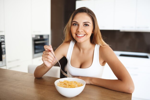 Attractive young girl eating cornflakes with milk smiling