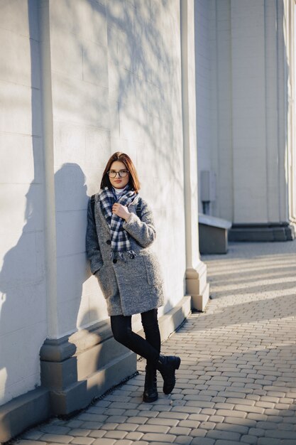 Attractive young girl wearing glasses in a coat walking on a sunny day