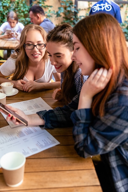 Attractive young girls are looking at the frontface of a modern smartphone at the cafe and smiling