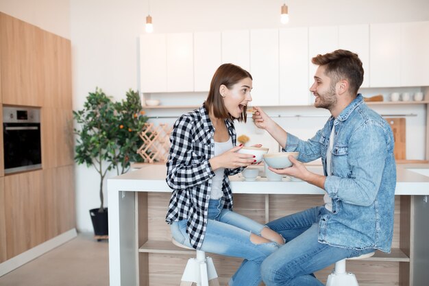 Attractive young happy man and woman in kitchen, eating breakfast, couple together in morning, smiling