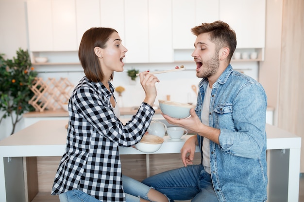 Attractive young happy man and woman in kitchen, eating breakfast, couple together in morning, smiling