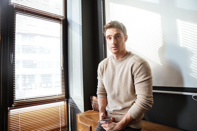 Attractive young man in office looking and using phone