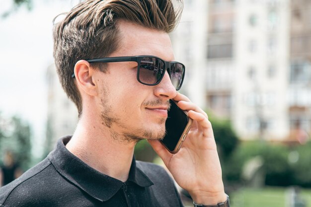 Attractive young man in sunglasses talking on a smartphone in the city