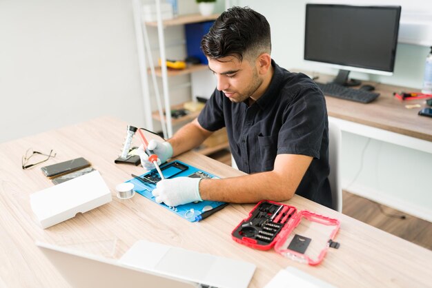 Attractive young man and technician using a soldering iron while trying to fix the hardware of a damaged smartphone