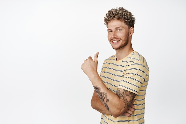 Free photo attractive young man with beard and curly blond hairstyle shows thumbs up with proud satisfied face smiling pleased praising and complimenting say yes like smth white background