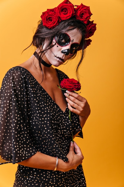 Attractive young woman affectionately , posing with beautiful red rose. Photo of girl with face art for carnival.