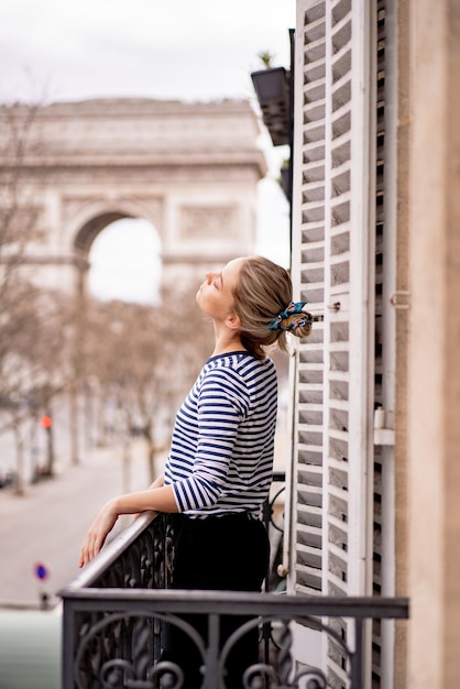 Free photo attractive young  woman on balcony in the morning in city paris. view of the triumphal arch.