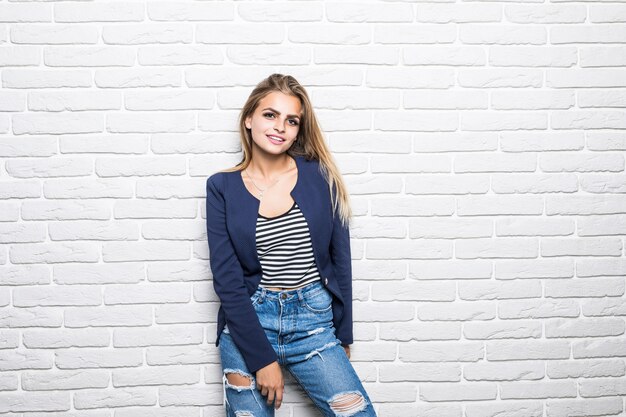 Attractive young woman in casual clothes looking and smiling on white brick wall