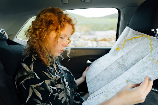 Free photo attractive young woman looking at map while sitting in car