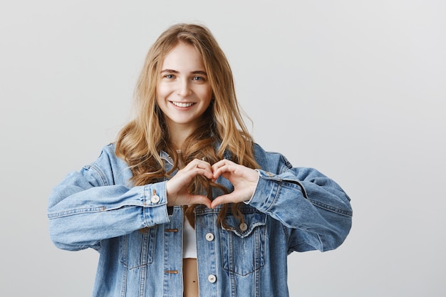 Attractive young woman showing heart gesture to express like, sympathy or love