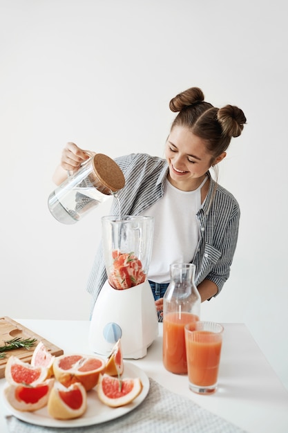 Free photo attractive young woman smiling adding water in blender with grapefruit pieces and rosemary. healthy diet food nutrition.