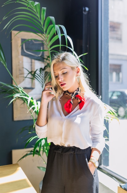 Free photo an attractive young woman standing near the window talking on cell phone with her hand in pocket