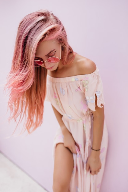 Free photo attractive young woman in trendy summer dress looking down while posing in studio.