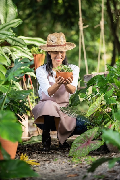 Attractive young woman working with decorative plants in garden center. female supervisor examining plants in gardening outside in summer nature. Beautiful gardener smiling. plant care.