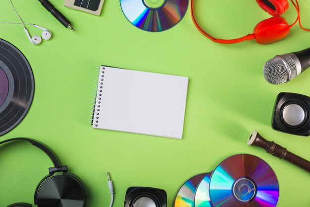 Audio equipments around the spiral blank notepad on green background