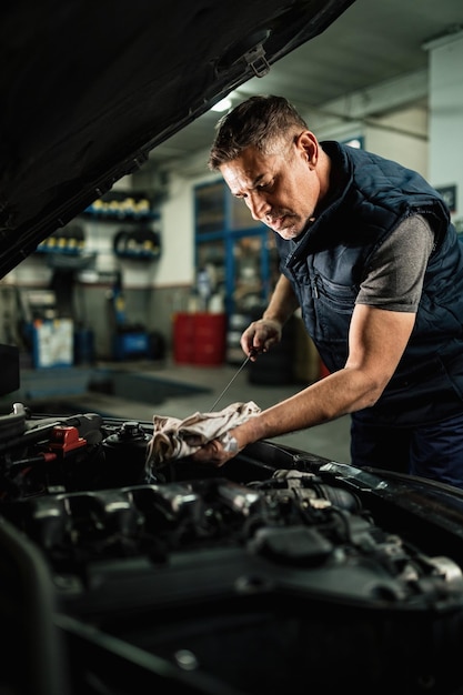 Auto mechanic checking oil in car engine while working in auto repair workshop