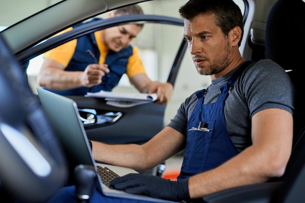 Auto mechanic running car diagnostic on laptop while working with colleague in auto repair shop