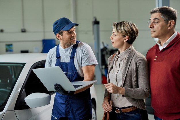 Auto repairman communicating with his customers while using laptop in a workshop