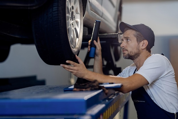 Free photo auto repairman using flashlight while examining car tire in a workshop