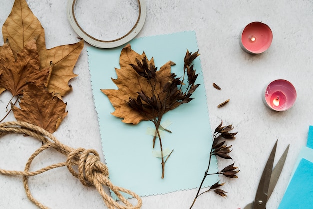 Autumn dry leaves on blue paper with string and lighted candles over the white backdrop