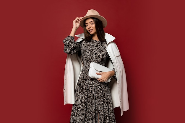 Free photo autumn fashion look. gorgeous european brunette gir in trendy white jacket and dress with print posing. holding leather handbag.