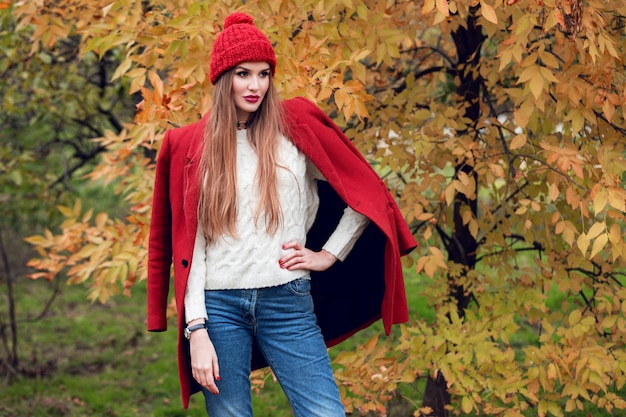 Free photo autumn fashion portrait of blonde woman in red stylish coat and knitted hat walking in park.