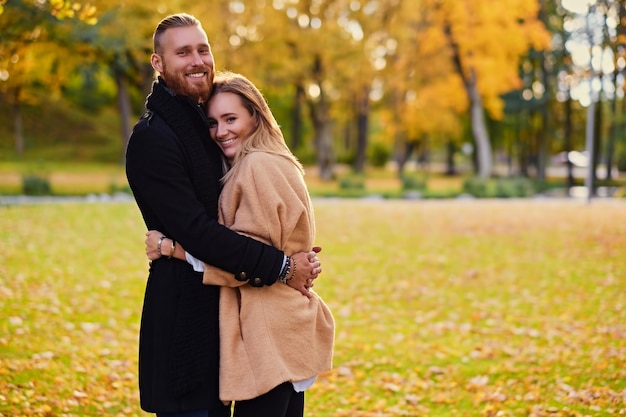 Autumn love story. Attractive redhead male hugs cute blonde female in autumn wild nature background.