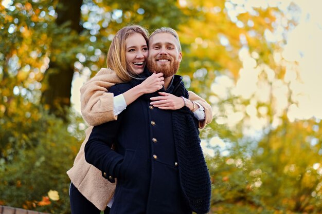 Autumn Love story. Redhead bearded male hugs the cute blonde female on the date in an autumn park.