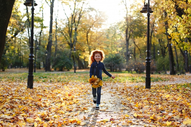 Free photo autumn vibes, child portrait. charming and red hair little girl looks happy walking and playing on t