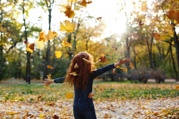 Autumn vibes, child portrait. Charming and red hair little girl looks happy walking and playing on t