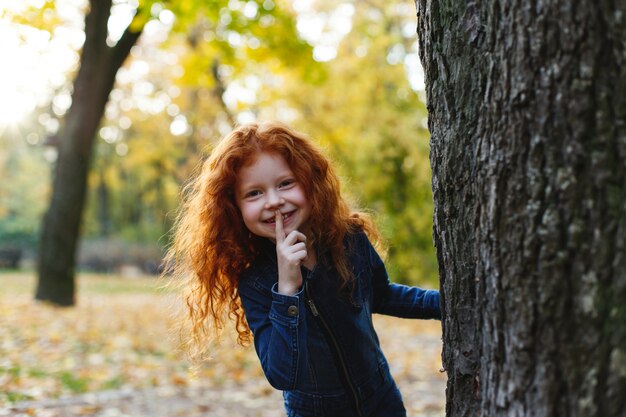 Autumn vibes, child portrait. Charming and red hair little girl looks happy walking and playing on t