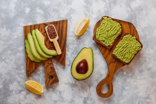 Avocado open toast with avocado slices, lemon, flax seeds, sesame seeds, black bread slices, top view