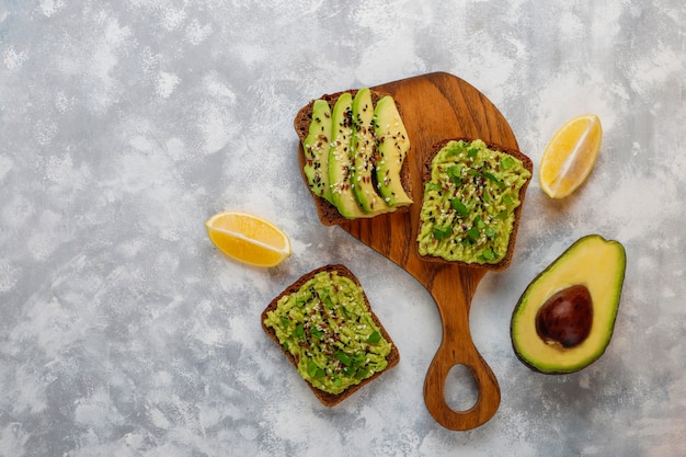 Avocado open toast with avocado slices, lemon, flax seeds, sesame seeds, black bread slices, top view