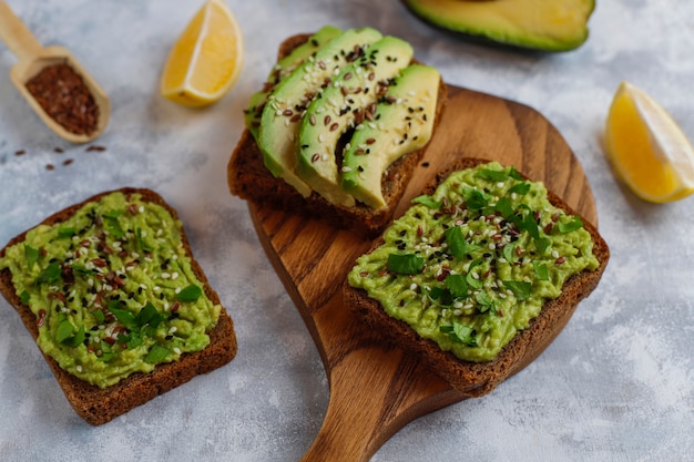 Avocado open toast with avocado slices, lemon, flax seeds, sesame seeds, black bread slices, top view