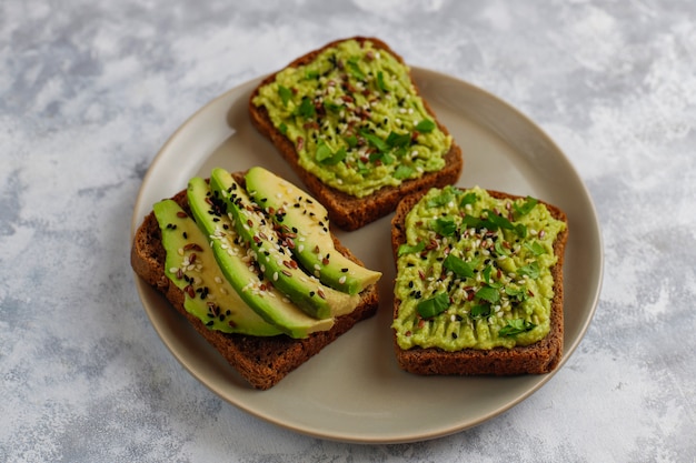 Avocado open toast with avocado slices, lemon, flax seeds, sesame seeds, black bread slices, top view