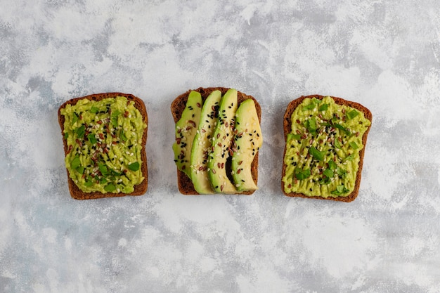 Avocado open toast with avocado slices, lemon, flax seeds, sesame seeds, black bread slices, top view